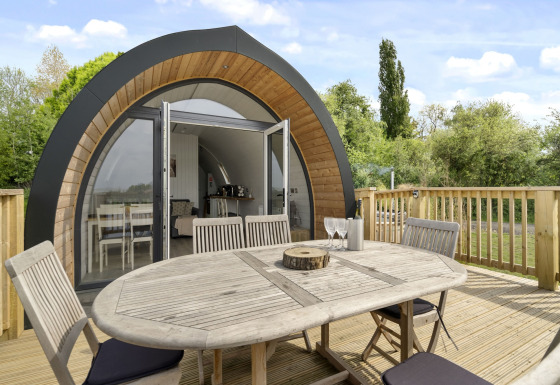 Buitenterras met tafel en stoelen voor The Highland Camping Pod, omringd door groene natuur.