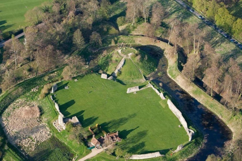 Luchtfoto van een oude kasteelruïne met grasvelden, bomen en stenen muren in het Verenigd Koninkrijk.
