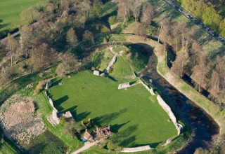 Luchtfoto van een oude kasteelruïne met grasvelden, bomen en stenen muren in het Verenigd Koninkrijk.