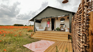 Safari-tent Foxley Lodge met buitenbad op houten terras, omgeven door klapvelden en rustieke buitendouche.