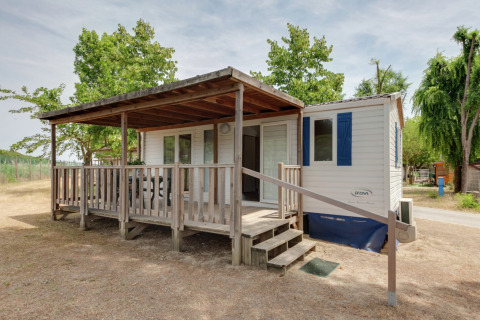 Casa móvil llamada Cottage Cesenatico con porche de madera cubierto y rampa, rodeada de naturaleza.