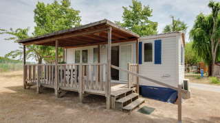 Mobilheim Cottage Cesenatico mit überdachter Holzterrasse, Rampe und Bäumen in einer ruhigen Umgebung.