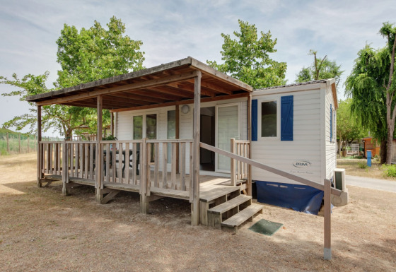 Mobilheim Cottage Cesenatico mit überdachter Holzterrasse, Rampe und Bäumen in einer ruhigen Umgebung.