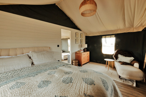 Slaapkamer in het Owls Nest safaritent in het Verenigd Koninkrijk met tweepersoonsbed en fauteuil.