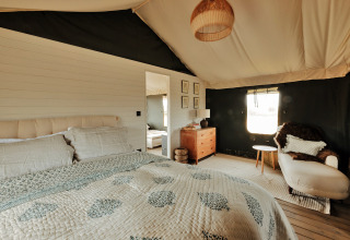 Slaapkamer in het Owls Nest safaritent in het Verenigd Koninkrijk met tweepersoonsbed en fauteuil.