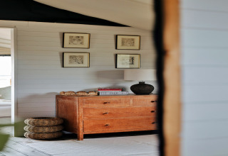 Interieur van de safaritent Owls Nest in het VK met houten ladekast, wandkunst en gevlochten manden.