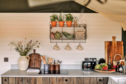 Gezellige keuken in safari tent Owls Nest, VK, met kruiden, planken, bloemen en moderne apparaten.