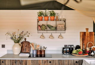 Gezellige keuken in safari tent Owls Nest, VK, met kruiden, planken, bloemen en moderne apparaten.