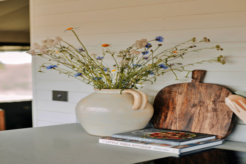 Decoratieve vaas met wilde bloemen, houten plank en kookboeken op het aanrecht in de Owls Nest safaritent.