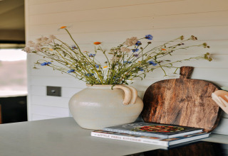 Decoratieve vaas met wilde bloemen, houten plank en kookboeken op het aanrecht in de Owls Nest safaritent.