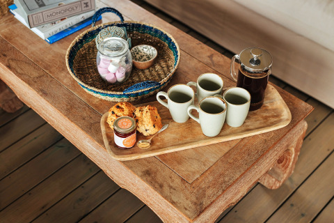 Koffieservies met vier mokken, een cafetière, scones en jam op een rustieke tafel in een safaritent.