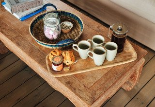 Koffieservies met vier mokken, een cafetière, scones en jam op een rustieke tafel in een safaritent.