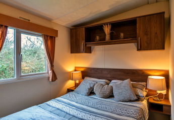Gemütliches Schlafzimmer im Chalet 'Phoenix Retreat', UK, mit Doppelbett, Holzregalen und Fensterblick.