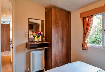 Schlafzimmer im Phoenix Retreat Chalet, Großbritannien, mit Holzschrank, Fenster und Blumenstrauß auf Regal.