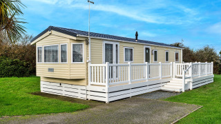 Afbeelding van het chalet Phoenix Retreat met ruim houten terras, gelegen op gras met een heldere blauwe lucht.