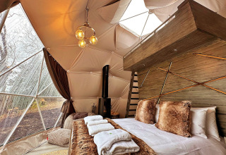 Luxury interior of Ashdown Luxury Dome in the UK featuring a cozy bed, fur pillows, and forest window view.