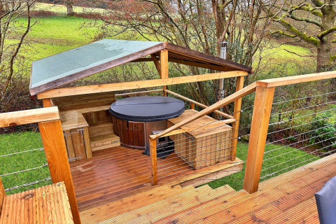 Outdoor deck with a covered hot tub and wooden benches at Ashdown Luxury Dome in the United Kingdom.