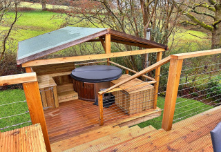 Outdoor deck with a covered hot tub and wooden benches at Ashdown Luxury Dome in the United Kingdom.
