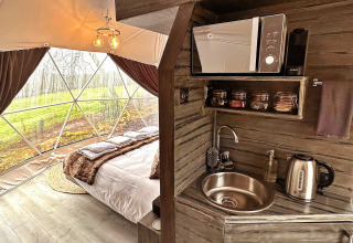 Interior view of Ashdown Luxury Dome in the UK, showing a cozy bed and small kitchenette with amenities.