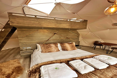Interior of the Ashdown Luxury Dome in the UK featuring a loft, cozy bed, towels, and elegant decor.