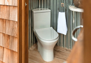 Modern toilet at Ashdown Luxury Dome, United Kingdom, with wood flooring and corrugated metal walls.