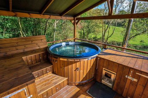 Outdoor wooden hot tub with scenic green views at Wakehurst Luxury Dome, United Kingdom, under a canopy roof.