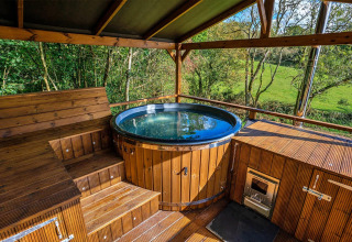 Outdoor wooden hot tub with scenic green views at Wakehurst Luxury Dome, United Kingdom, under a canopy roof.