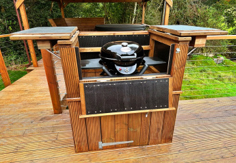Houten buitenkeuken met grill op terras bij Wakehurst Luxury Dome, Verenigd Koninkrijk, in groene omgeving.