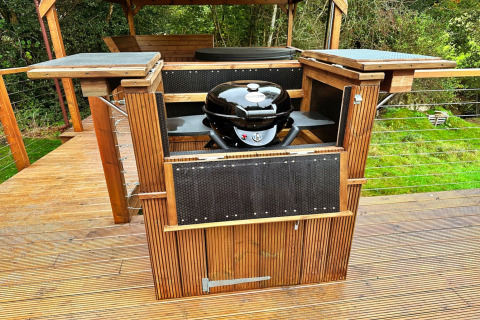 Buitenbarbecue in hout op het terras bij Wakehurst Luxury Dome, Verenigd Koninkrijk, omringd door groen.