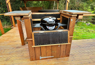 Buitenbarbecue in hout op het terras bij Wakehurst Luxury Dome, Verenigd Koninkrijk, omringd door groen.
