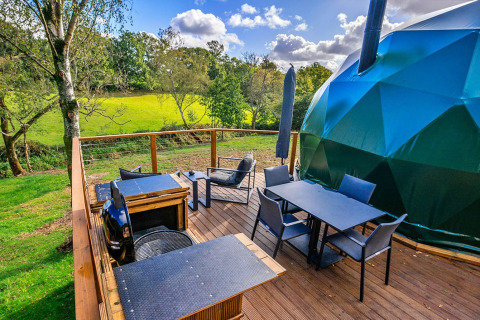 Buitenterras naast Wakehurst Luxury Dome in het Verenigd Koninkrijk met zitplaatsen en uitzicht op natuur.