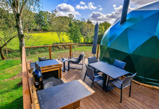 Outdoor deck at Wakehurst Luxury Dome in the UK with seating, dining table, and views of green fields.