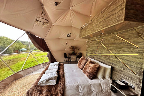 Binnenkant van Wakehurst Luxury Dome in het VK met fraai bed, moderne inrichting en groene panorama’s.