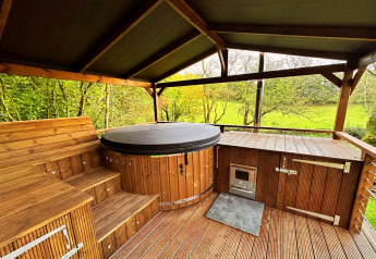 Overdekt houten terras met bubbelbad en groen uitzicht bij Wakehurst Luxury Dome, Verenigd Koninkrijk.