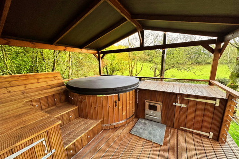 Covered wooden patio with a hot tub and scenic countryside view at Wakehurst Luxury Dome, United Kingdom.