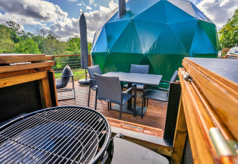 Buiten terras met barbecue en eettafel voor de Wakehurst Luxury Dome, omgeven door natuur in het VK.