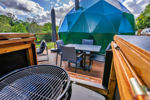 Buitenterras met barbecue en eettafel bij de Wakehurst Luxury Dome, omringd door natuur, Verenigd Koninkrijk.