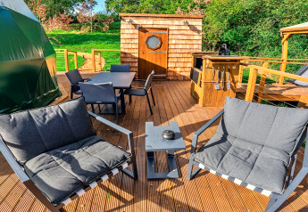 Buitenterras bij Wakehurst Luxury Dome, VK, met moderne stoelen, eettafel en barbecuegedeelte.