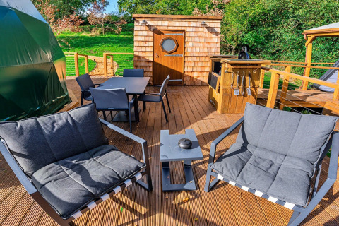 Outdoor deck at Wakehurst Luxury Dome, UK, featuring modern seating, dining table, and BBQ grill area.