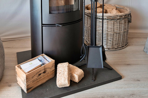 Wood stove with firewood briquettes, tools, and a basket in Ashdown Luxury Dome, United Kingdom.