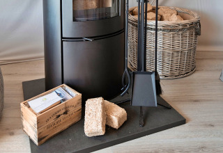 Wood stove with firewood briquettes, tools, and a basket in Ashdown Luxury Dome, United Kingdom.