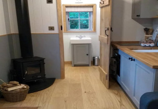Gezellig interieur van The Bakers Hut stacaravan in het VK met houtkachel, keuken en wastafelgedeelte.