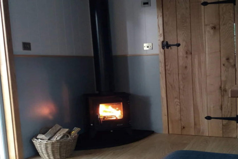 Knus hoekje in The Bakers Hut, een mobile home in het VK met houtkachel, houten deur en houtmand.