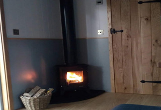 Knus hoekje in The Bakers Hut, een mobile home in het VK met houtkachel, houten deur en houtmand.