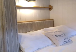 Knusse slaapkamer in The Bakers Hut mobiele woning in het VK, met gestreept hoofdbord en zachte kussens.