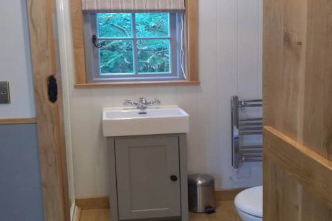 Kleine badkamer in een mobiele woning genaamd ‘The Bakers Hut’ in het VK, met wasbak, toilet en raam.