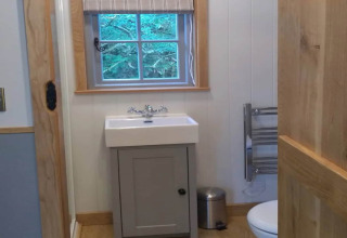 Kleine badkamer in een mobiele woning genaamd ‘The Bakers Hut’ in het VK, met wasbak, toilet en raam.