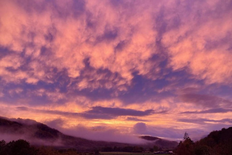 Zonsondergang bij The Bakers Hut in het VK, met velden en heuvels onder roze en paarse wolken.