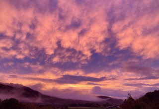 Zonsondergang bij The Bakers Hut in het VK, met velden en heuvels onder roze en paarse wolken.