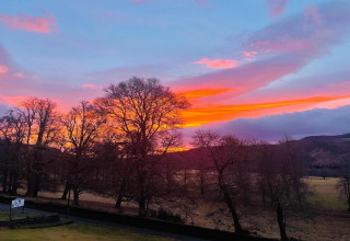 Kleurrijke zonsondergang achter kale bomen bij The Bakers Hut mobilhome in het VK, landelijke omgeving.